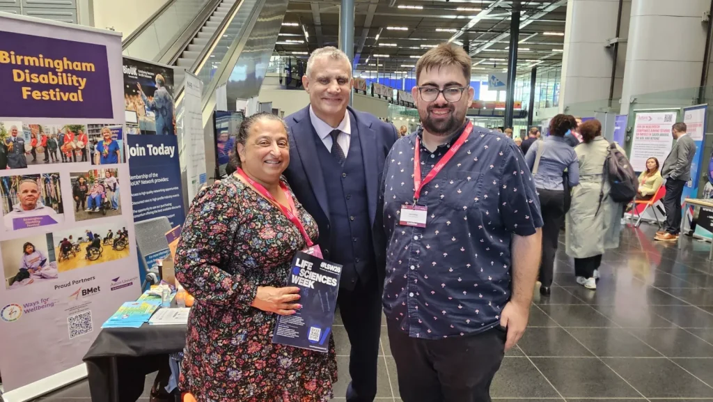 Paul Cadman with two visitors at the Life Sciences Week 2026 exhibition, beside the Birmingham Disability Festival stand