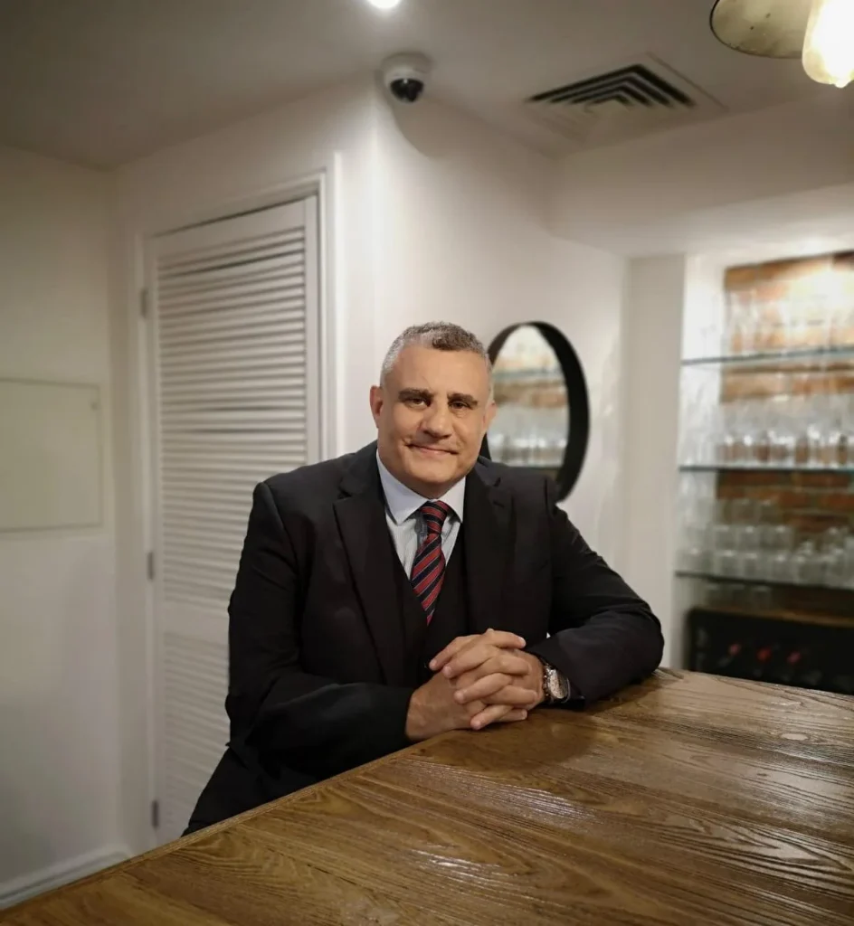 Paul Cadman seated at a wooden table in a dark suit