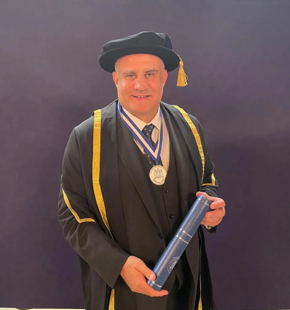 Professor Paul Cadman in academic robes holding a degree scroll